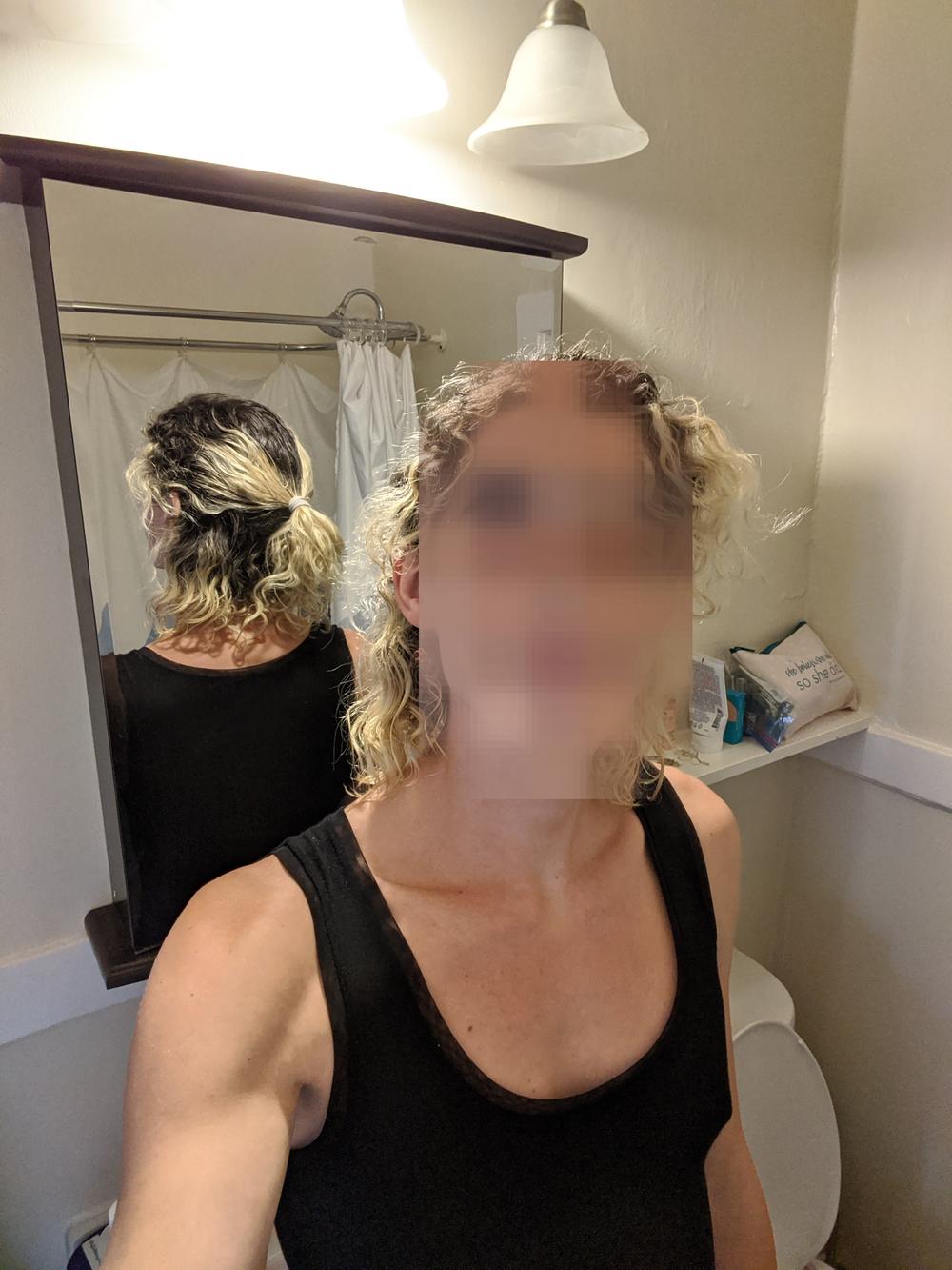 Une personne faisant dos à un miroir de salle de bain regarde directement la caméra. Son visage est embrouillé comme une censure.