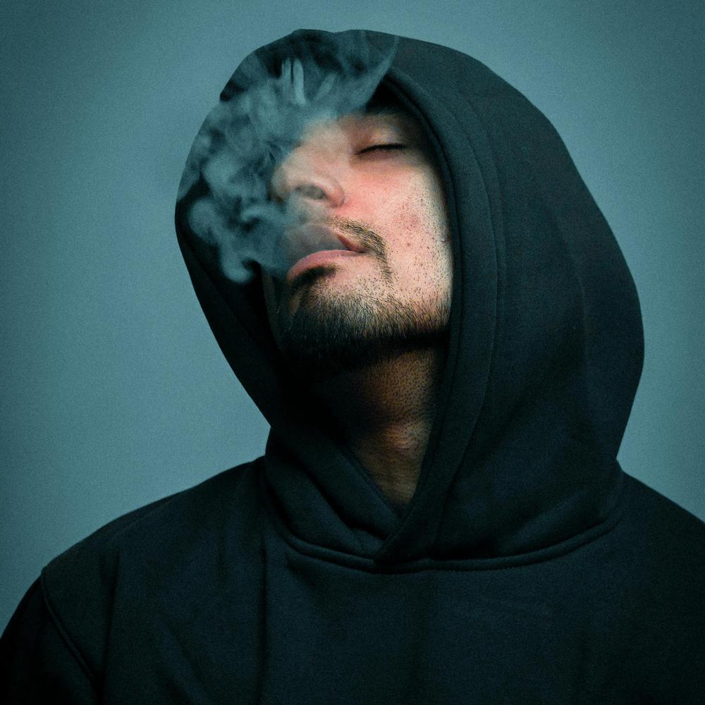 De la fumée sort de la bouche d'un homme portant un chaidail et u capuchon.