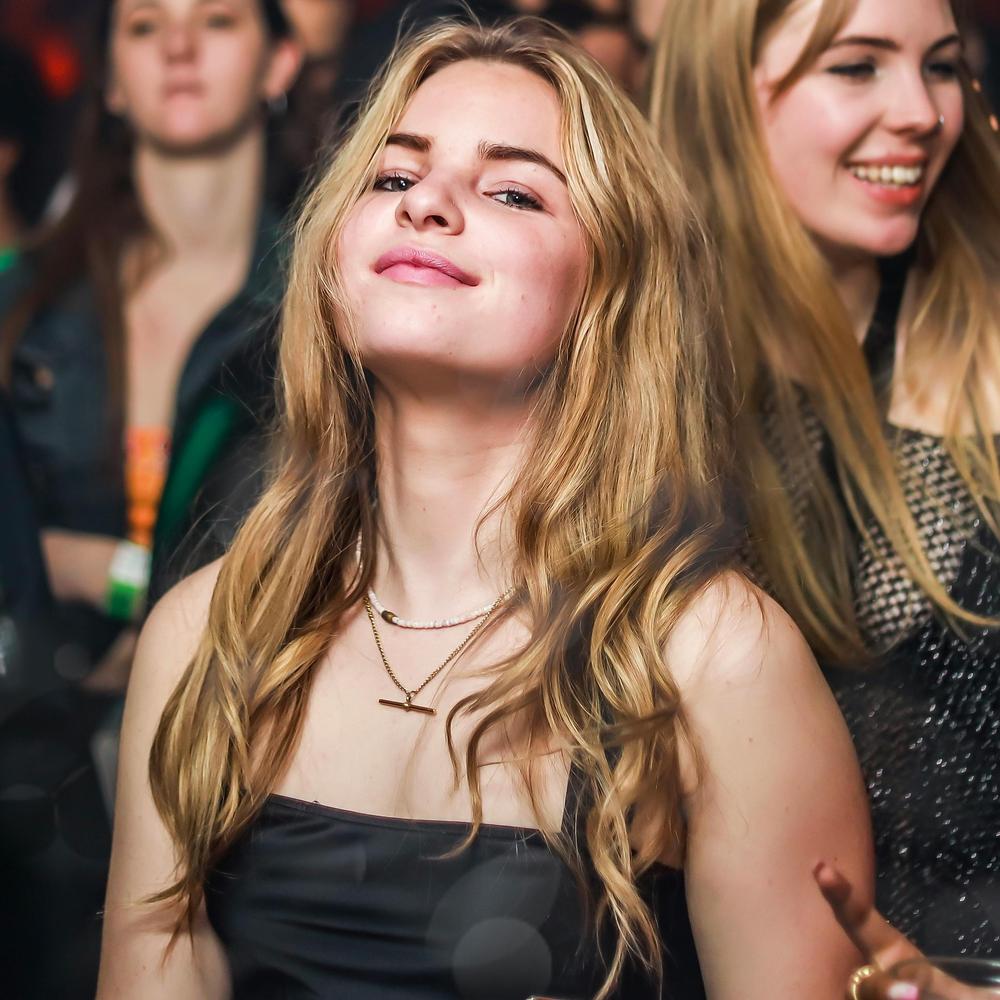 Une femme au milieu d'une piste de danse dans un festival regarde la caméra en souriant.