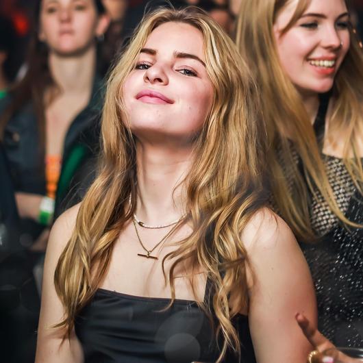 Une femme au milieu d'une piste de danse dans un festival regarde la caméra en souriant.